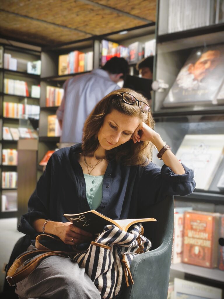 a woman reading a book in an armchair at a bookstore with book shelves on the background