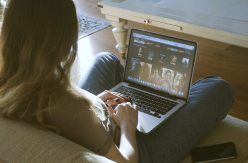 a woman sitting on the couch browsing movies on her laptop