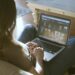 a woman sitting on the couch browsing movies on her laptop